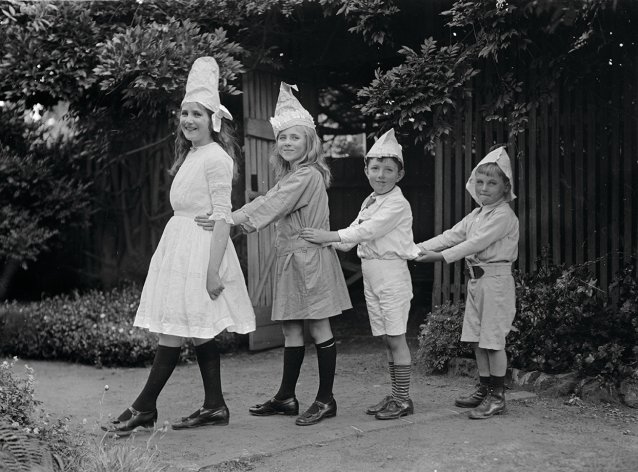 Two girls and two boys wearing party hats, standing in line