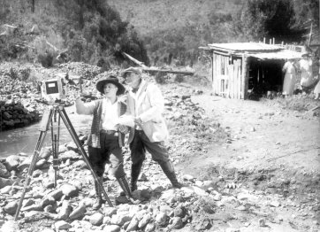 Louise Lovely and Wilton Welch setting up a camera on a rocky river bank by John H Robinson
