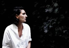 Angelica Mesiti in profile wearing a white linen shirt in front of a dark leafy hedge