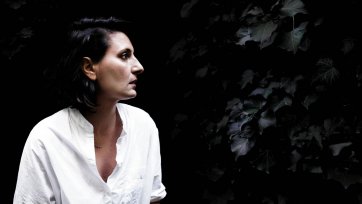 Angelica Mesiti in profile wearing a white linen shirt in front of a dark leafy hedge