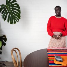 Atong Atem standing behind a wooden table and next to a large leafy green plant