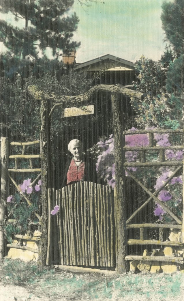 Marie Bjelke Petersen standing at the timber gate in her garden at ‘Sylvan Fells’, 1940s