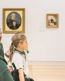 A teacher with a group of children in front of a painting in a gallery