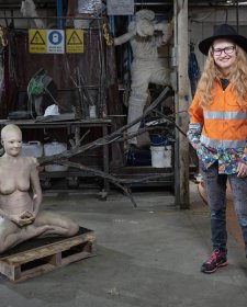 Nell standing in her workshop next to a cross legged sculpture