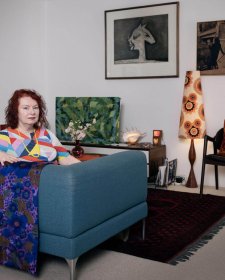 Deborah Kelly sitting on a blue couch in a room with artworks on the walls