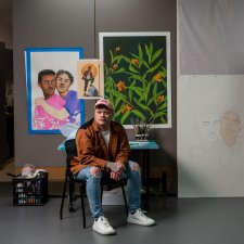 Dylan Mooney sitting on a chair in front of a wall with paintings and drawings